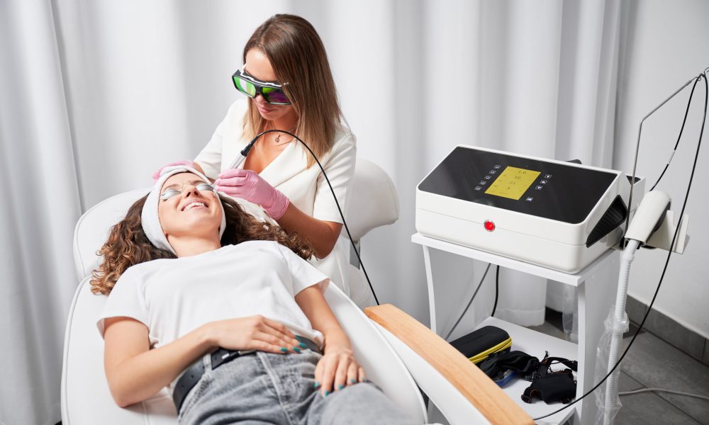 Modern hardware cosmetology. Laser removal of small vessels on face. Modern treatment of telangiectasias on skin. Beautician performing local high-precision removal of dilated small vessels on face with innovative yellow laser.